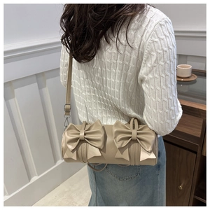 Detail einer beige Zylindertasche mit Doppelschleifen an einem Model im weißen Pullover