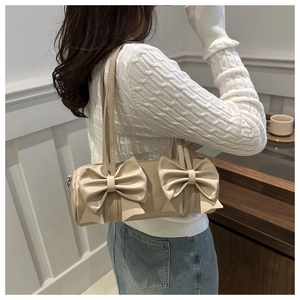 Detail der cremefarbenen Zylindertasche mit großen Doppelschleifen und Schultergurt