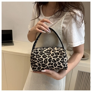 Detailed close-up of leopard print canvas fabric and black leather handle on mini bag