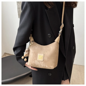 Detail view of khaki dumpling bag with decorative patch and plush ball charm on model