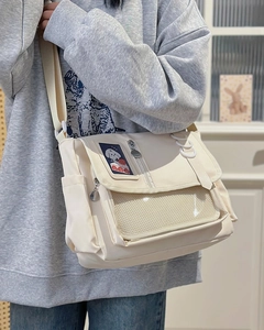 Detail view of the cream canvas messenger bag with a cute dog patch and white mesh pocket