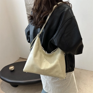 Minimalist beige hobo shoulder bag with geometric stitching shown on model in modern interior