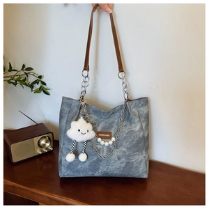 Detail of gray canvas tote bag featuring brown leather straps and plush cloud charm