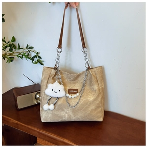 Detail of khaki tote bag with plush cloud charm and pearl chain on a vintage stool