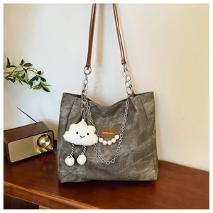 Olive green tote bag with metal chain strap and white plush cloud charm on a wooden table