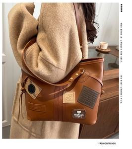 Detail of amber brown tote bag with decorative patches and golden hardware on beige coat
