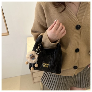 Detail of a shiny black pleated leather handbag with a plush charm and gold logo