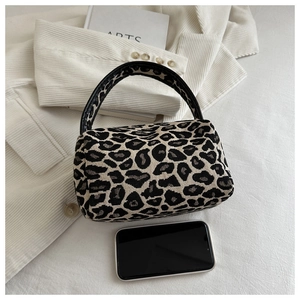 Detail shot of leopard print cylindrical handbag on corduroy jacket with artsy book background