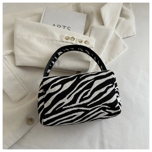 Detailed close-up of a mini zebra pattern handbag on a white textured blazer background