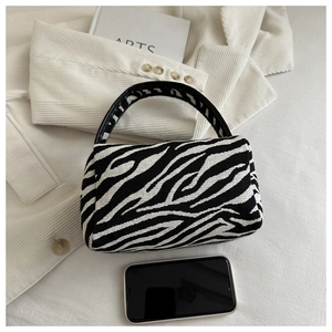 Detail view of a zebra print mini pillow bag with black handles and a phone for scale
