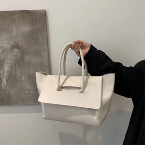 Borsa tote minimalista in pelle crema con design alato mostrata tenuta da una modella