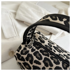 Close-up of leopard print woven handbag featuring a black zipper and leather handle