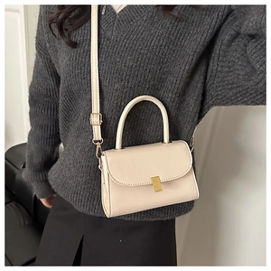 Détail d'un sac bandoulière beige en cuir avec fermoir doré porté sur un pull gris