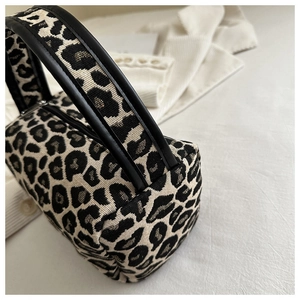 Detail of leopard print fabric texture and leather handle on a mini barrel bag