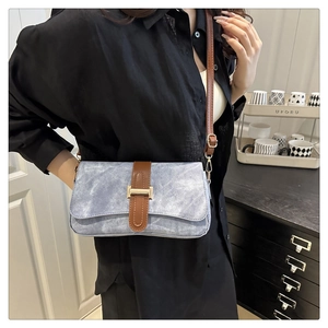 Détail du sac bandoulière en denim bleu avec bandoulière en cuir brun et boucle dorée