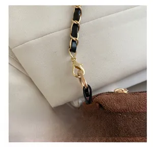 Detail of brown suede bag featuring gold lobster clasp and black leather chain strap