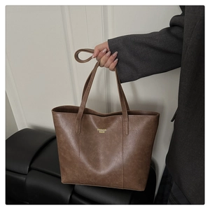 Gros plan d'un sac cabas marron texture vintage avec logo doré porté à la main