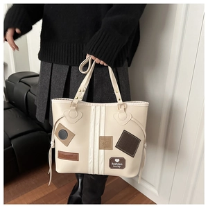 Detail of cream leather tote bag featuring fashion lucky patches and stylish side tassels
