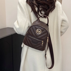 Brown mini quilted backpack with gold M logo on a model wearing a white coat