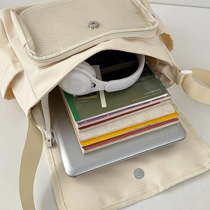 Detail view of large capacity cream canvas messenger bag holding laptop and headphones