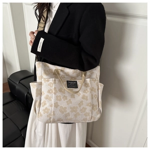 Detail view of multi-pocket canvas tote bag featuring yellow floral prints and brand label