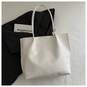 Detail of white woven tote bag with slim shoulder straps on a black blazer backdrop