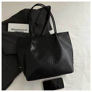 Detail view of black embossed tote bag with woven texture on a minimalist white backdrop