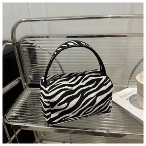 Close-up of zebra print mini pillow bag featuring glossy black handle and silver zipper detail