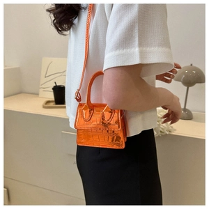 Mini metallic orange crocodile embossed crossbody bag styled on a white textured top