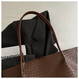 Detail of dark brown woven leather tote bag with elegant handles and textured pattern