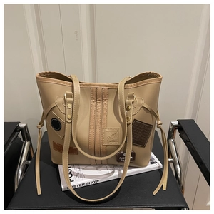 Detailed close-up of a beige faux leather tote bag with vintage patches and long fringe charm