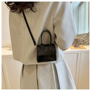 Detail view of mini black faux crocodile leather handbag worn by model with braided strap