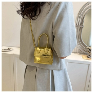 Macro detail of mini gold metallic handbag with crocodile embossed pattern on model back
