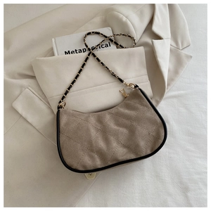 Detail of khaki quilted chain bag with black trim placed on a beige blazer with a book