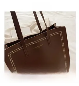 Detail of dark brown pebble leather tote bag with white contrast stitching and gold logo