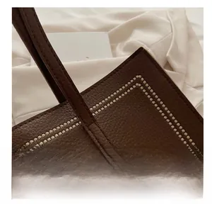 Close-up of brown pebbled leather tote bag with white stitching and gold logo detail