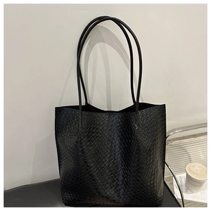 Detail showing black woven tote bag texture and long shoulder strap in a modern setting