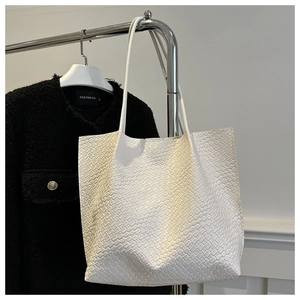 Detailed close-up of woven texture on a white leather tote bag hanging on a metal stand
