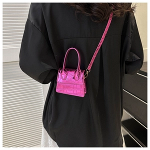 Detail of a hot pink micro handbag with crocodile texture and long shoulder strap