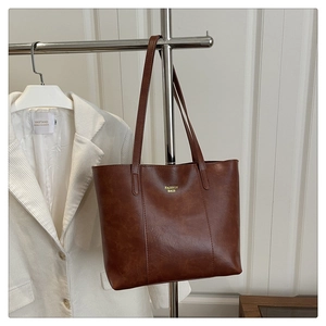 Sac fourre-tout marron foncé mat avec lettrage doré à côté d'un blazer en velours blanc