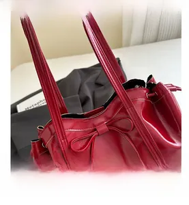 Close-up of red glossy leather tote bag featuring a decorative bow and drawstring detail