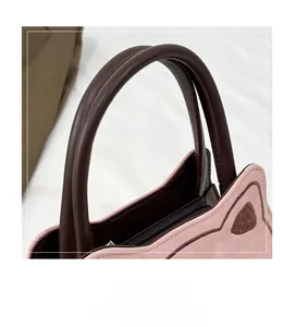 Detail view of pink suede cat-ear handbag showing brown leather handle and zipper closure