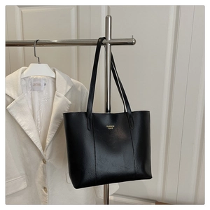 Détail du sac cabas en cuir PU noir avec lettrage doré suspendu sur un support métallique