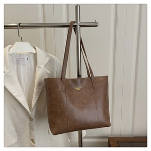 Détail du sac cabas en cuir marron vintage avec lettrage doré sur un support en métal