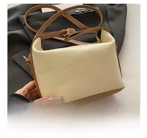 Close-up of cream textured shoulder bag with pleated fabric and brown adjustable strap
