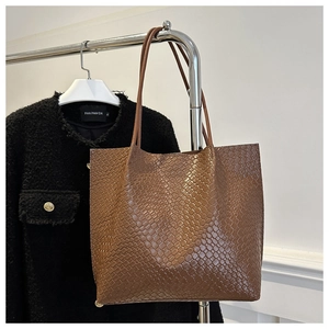 Detail of a brown woven leather tote bag with a high-gloss finish and slim straps