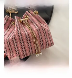 Close-up of pink tweed bucket bag with woven texture, golden chain, and pearl charms