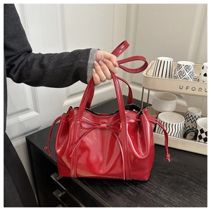 Detail of red patent leather tote bag featuring a bow decoration and drawstring sides
