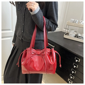 Detailed view of red patent leather tote bag with bow accent and drawstring on model
