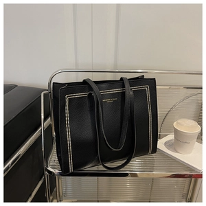 Detail of black pebbled leather tote bag with gold rivet accents and metallic rack